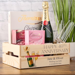 May include: A wooden crate gift set containing a bottle of Moët champagne, two champagne flutes, and boxes of chocolates. The crate is decorated with a champagne bottle and glasses illustration and the text "Happy 40th Anniversary".