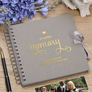 May include: Gray spiral bound memory book with a gold foil heart and the words "In Loving Memory" in a gold script font. The book has a gray ribbon closure and the text "Phyllis Rose Marshall Died May 20th, 2024" is printed in gold foil.
