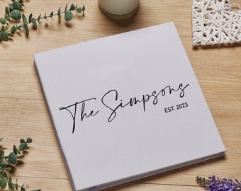 May include: A white photo album with the text "The Simpsons EST. 2023" printed on the cover.