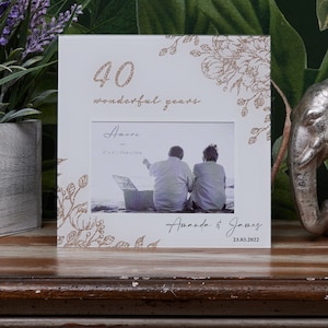 May include: White picture frame with a gold glitter design. The frame has a 15cm x 10cm photo opening and says "40 wonderful years" and "Amore" on the front. The frame also has a personalized message that says "Amanda & James 23.03.2022".