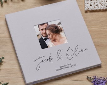 May include: A grey wedding photo album with a window showing a photo of a couple. The album has the text "Jacob & Olivia" and "22nd May 2022 Somerset House London" printed on the front.