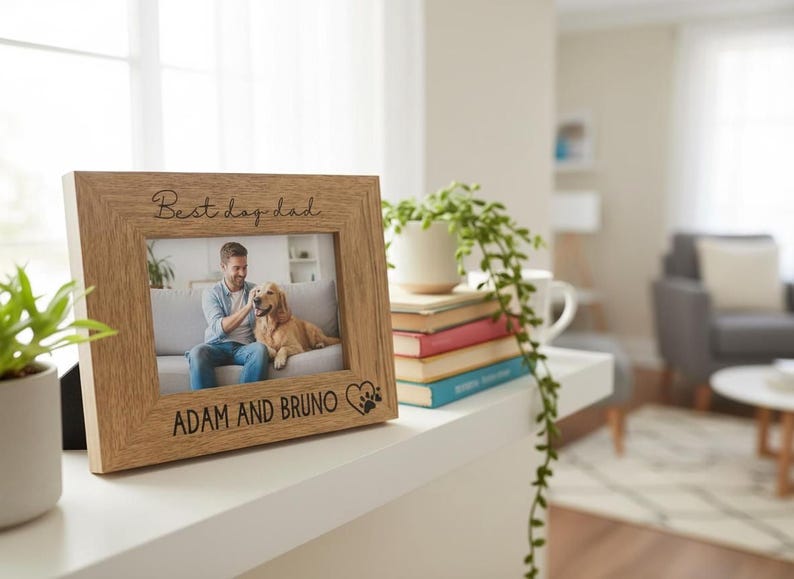 A wooden picture frame with a photo of a man and a dog, along with the text "Best day dad" and "Adam and Bruno" engraved on it, sits on a shelf in a living room.