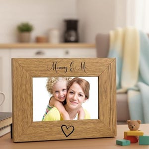A wooden picture frame with a photo of a woman and a child inside, placed on a table with a coffee mug and some books.