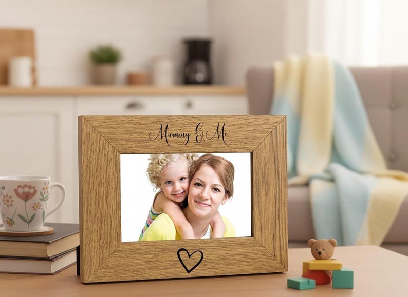 A wooden picture frame with a photo of a woman and a child inside, placed on a table with a coffee mug and some books.