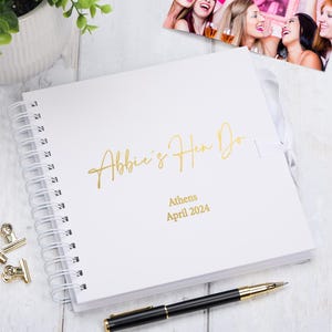 Könnte beinhalten: Weißes Gästebuch mit Spiralbindung und goldener Schrift "Abbie's Hen Do" und "Athen April 2024".