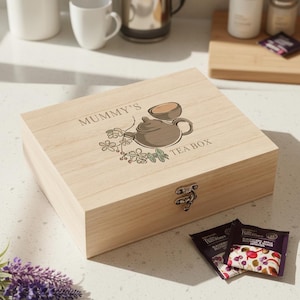 May include: A wooden tea box with the words "MUMMY'S TEA BOX" printed on the lid. The lid features a teapot and teacup illustration with floral accents. Two tea bags are visible in the foreground.
