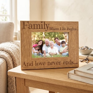 A wooden picture frame with a family photo inside, placed on a wooden table. The frame has a message engraved on it that says "Family Where Life Begins... And love never ends..."