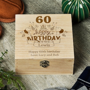 May include: A wooden box with a hinged lid and a metal clasp. The box is engraved with the text "60 happy birthday to you Lewis", along with a birthday cake, balloons, and stars. The bottom of the box is engraved with the text "Happy 60th birthday Love Lucy and Rob".