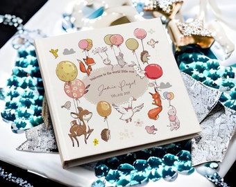 May include: A white baby photo album with a colorful illustration of animals and balloons. The text on the cover reads "Welcome to the world little one, Jamie Paget, 17th July 2021".