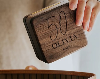 Puede incluir: Una caja de madera con tapa abatible, grabada con el número "50" y el nombre "Olivia".