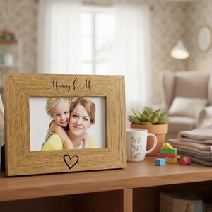 A wooden picture frame with a photo of a woman and a child, along with a heart symbol, sits on a wooden shelf in a cozy living room.