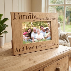 A wooden picture frame with a family photo inside, placed on a wooden dresser. The frame has a message engraved on it that says "Family Where Life Begins... And love never ends..."