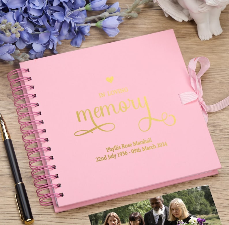 May include: Pink spiral bound memory book with a gold ribbon and the words "In Loving Memory" and "Phyllis Rose Marshall 22nd July 1936 - 09th March 2024" in gold lettering.