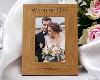 May include: A wooden picture frame with the text "Wedding Day" engraved on the top. The frame has a small heart design at the bottom and a photo of a bride and groom inside.