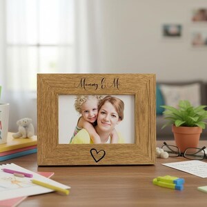 a wooden picture frame with a photo of a woman and a child, placed on a desk with various items such as a coffee mug, a plant, and some papers.