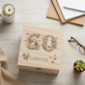 May include: A wooden box featuring the number "60" decorated with flowers and butterflies, with the name "Catherine" printed below. The floral design includes pink, yellow, and green hues. The box has a metal clasp.