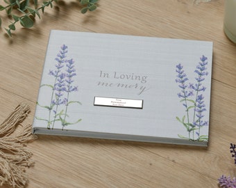 May include: A white linen-textured memory book with a lavender floral design. The book has a silver label that says "In Loving Memory" and a space for a personalized text.