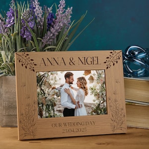 May include: A wooden photo frame with a floral design and the text "Anna & Nigel" and "Our Wedding Day 23.04.2025". The frame has a photo of a couple in a wedding setting.