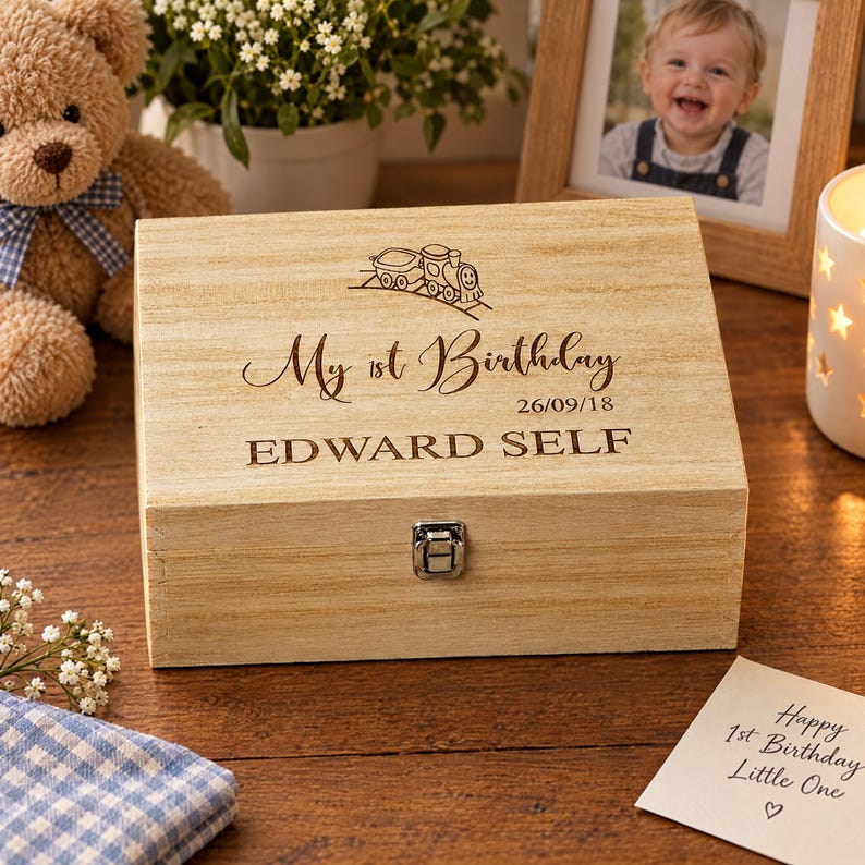 A wooden box with a personalized message engraved on it, placed on a wooden surface next to a teddy bear, a picture frame, and a candle.