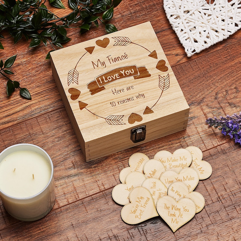 May include: Wooden box with a lid, engraved with the words "My Fianc&eacute; I LOVE YOU Here are 10 reasons why". The box is decorated with hearts and arrows. The box contains small wooden hearts with engraved messages.