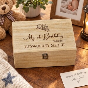 A wooden box with a personalized message engraved on it, sitting on a wooden surface next to a teddy bear and a framed photo.