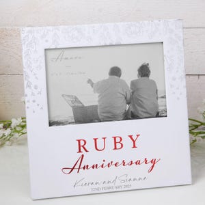 May include: White photo frame with a silver floral design. The frame has a 6x4 inch opening and says "Ruby Anniversary" in red lettering. The text below says "Kieran and Sianne" and "22nd February 2025".