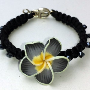 May include: A black elastic hair tie with a black flower charm. The flower has yellow and white petals.