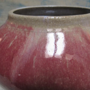 May include: A large, round ceramic pot with a red and white glaze. The pot has a wide opening and a smooth, glossy finish.