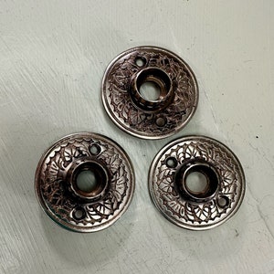 May include: Three silver door knobs with intricate floral designs. The knobs have a circular shape and a central hole for a door handle.