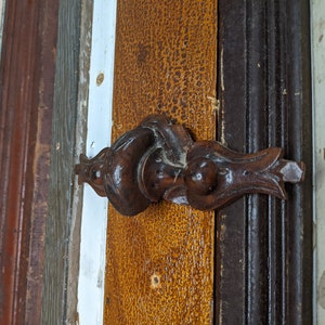 May include: A close-up of a dark brown wooden door handle with intricate carvings. The handle is attached to a wooden door with multiple layers of paint.