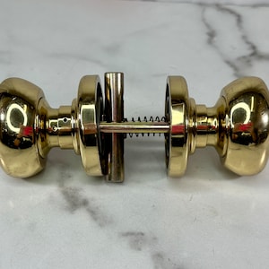 May include: A pair of polished brass door knobs with a spring mechanism connecting them.