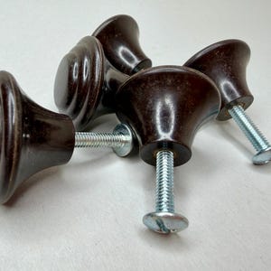 May include: A set of five dark brown cabinet knobs with a glossy finish. Each knob has a rounded, ridged design and is attached to a silver screw. The knobs are likely for furniture restoration or new construction.