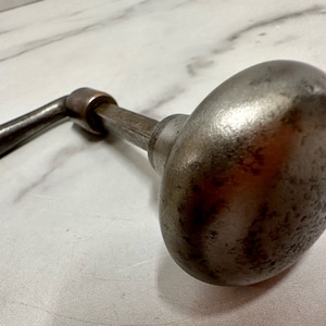 May include: A vintage, silver-toned door knob with a lever handle. The knob has a textured surface and a rounded shape.