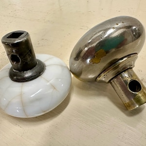 May include: Two antique door knobs. One is white porcelain with a metal base and the other is silver with a brass base.