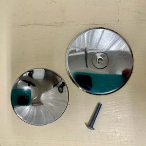 May include: Two silver metal round covers with a screw. The larger cover has a small hole in the center. The smaller cover has a slight curve in the center.