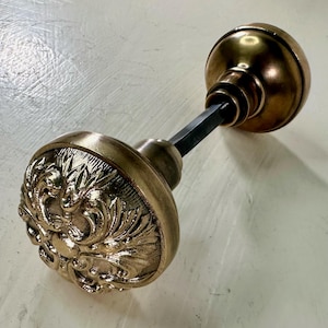 May include: A vintage brass door knob with an ornate floral design. The knob is in excellent condition and has a beautiful patina.