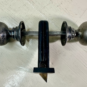 May include: Antique door knob set with two spherical knobs and a connecting rod. The knobs are a tarnished silver color, and the set includes a black metal mortise lock. The hardware is designed for a door.