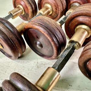 May include: A set of six antique wooden door knobs with brass accents. The knobs are round and have a detailed design. The knobs are connected by a metal rod.