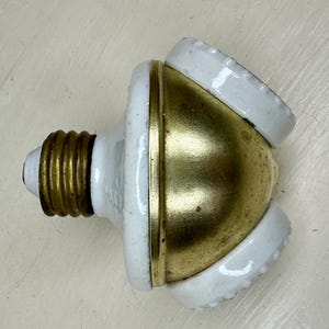 May include: A vintage light bulb adapter with a brass finish and three white porcelain sockets. The adapter has a standard E26 base and is designed to split a single light socket into multiple bulbs.