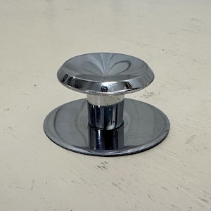 May include: A chrome-plated sink drain stopper with a round, flat base and a raised, conical top.