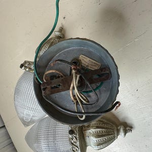 May include: An antique ceiling light fixture with two glass shades. The fixture has a metal base and decorative, off-white accents. Exposed wiring and a green ground wire are visible.