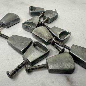 May include: A group of nine silver-toned cabinet knobs with a unique, slightly curved, triangular shape. Each knob has a screw hole and a small, round opening on the top.