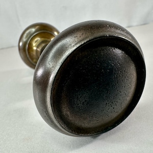 May include: A vintage door knob with a round, dark gray metal handle and a brass base.