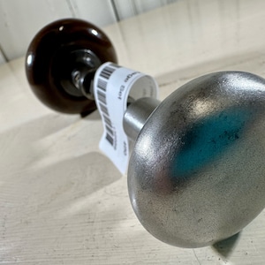 May include: A silver door knob with a brown wooden base. The knob is round and has a smooth surface. The base is also round and has a textured surface.