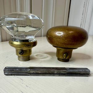 May include: Two antique door knobs, one clear faceted glass and the other a rounded brass. A metal tap and die tool is also present. The knobs have brass bases and are likely vintage hardware.