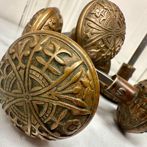 May include: Close-up of antique bronze door knobs with intricate floral and leaf patterns. The knobs have a weathered appearance, showcasing detailed craftsmanship. The hardware is likely for interior doors.