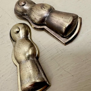 May include: Two antique gold-toned metal door handles with a rounded, bulbous shape. The handles have a distressed finish and are designed to be used on cabinet doors.