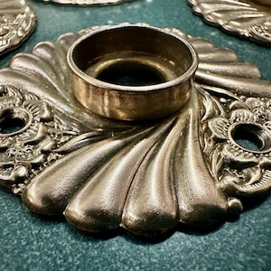 May include: A silver-toned metal door knob with a decorative floral design and a round, smooth center. The knob has a raised edge and a slightly textured surface.