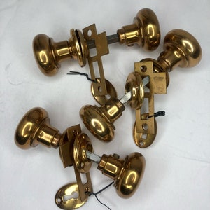 May include: Four antique brass door knobs with keyholes and plates. The knobs are round and have a smooth, polished finish.