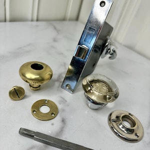 May include: A vintage door knob set with a clear glass knob, brass knob, and a silver plated backplate. The set includes a spindle, a screw, and two decorative plates.